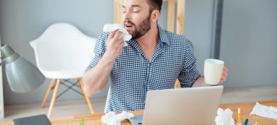 Sneezing man at his desk surrounded by tissues.