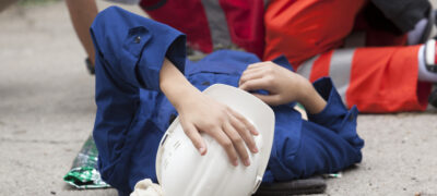 Person in hardhat lying on ground holding their head.